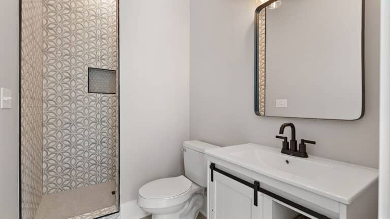 Modern bathroom vanity with black hardware, square mirror, and decorative tile shower in a Wingfield Estates custom home
